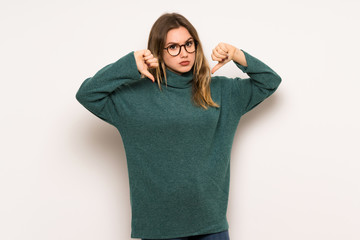 Teenager girl over white wall showing thumb down with both hands