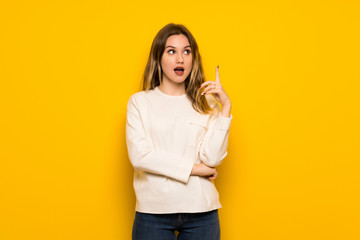 Teenager girl over yellow wall thinking an idea pointing the finger up