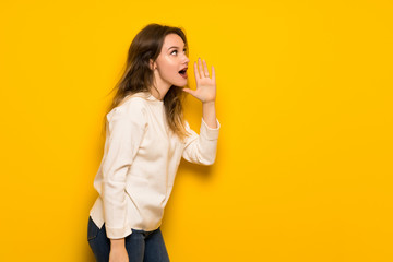 Teenager girl over yellow wall shouting with mouth wide open to the lateral