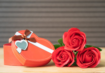 Red roses and heart-shaped box on wood background