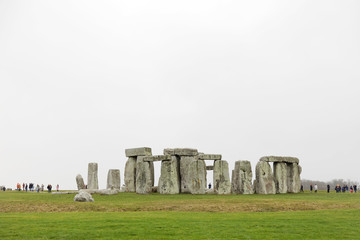 Tourists watching the stone monument Stonehenge a cloudy day,  built in the late Neolithic period,...