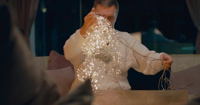 Senior adult Caucasian male trying to unravel the garland at home. 4K UHD 60 FPS SLOW MOTION Blackmagic RAW