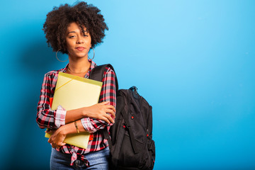 young african student with backpack on the back on blue background - obrazy, fototapety, plakaty