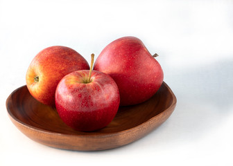 Three red apples on the wooden plate and white background