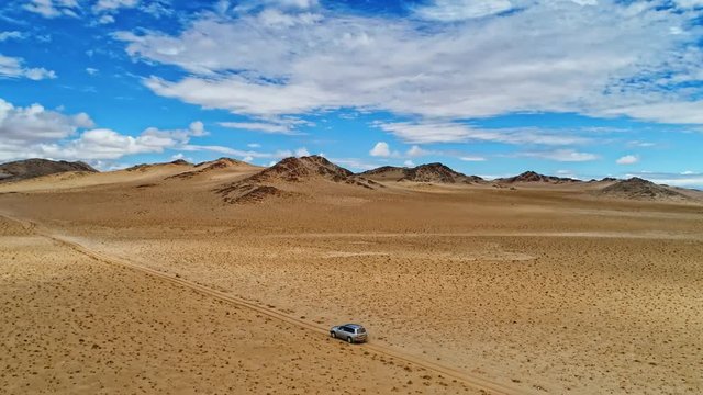 Aerial footage of car overcoming sandy dunes racing on desert off roads, bird's eye view of truck driving on sandy lands of desert