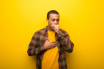Young african american man on vibrant yellow background is suffering with cough and feeling bad