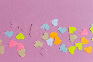 Many colorful paper heart shaped confetti on pink lilac purple background. Valentine's concept card with copyspace.