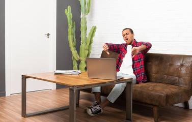 African american man with laptop in the living room showing thumb down with both hands