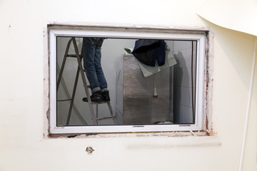 Worker in uniform stands on stepladder in window opening. Concept construction team, finishing works, redecoration, cabinet reconstruction, window changing, repair suspended ceiling
