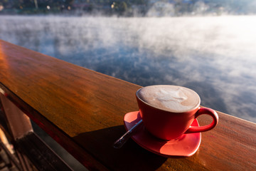 A cup of coffee on wooden table with steam over lake at Rakthai village, Mae Hong Son, Thailand