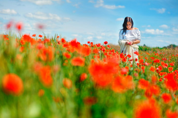 Obraz na płótnie Canvas Beautiful girl walks in a poppy field, holding petals in her hands, spring mood
