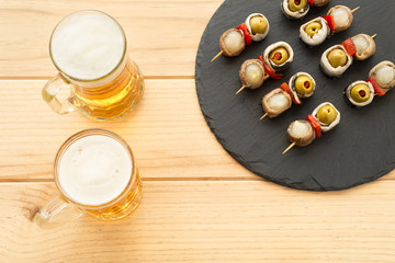 Plato de banderrillas y dos jarras de cerveza sobre una mesa de madera. Típica tapa española. 