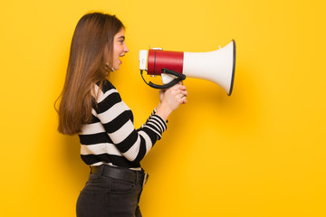 Young woman over yellow wall shouting through a megaphone to announce something in lateral position