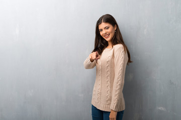 Teenager girl with sweater on a vintage wall points finger at you with a confident expression