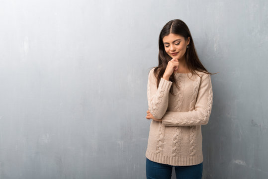 Teenager girl with sweater on a vintage wall looking down with the hand on the chin