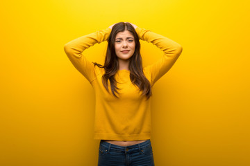 Teenager girl on vibrant yellow background takes hands on head because has migraine