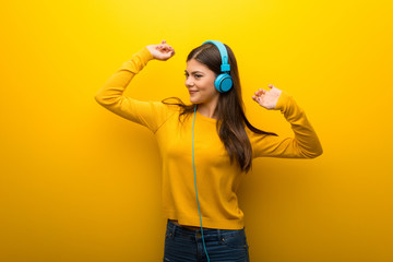 Teenager girl on vibrant yellow background listening to music with headphones and dancing