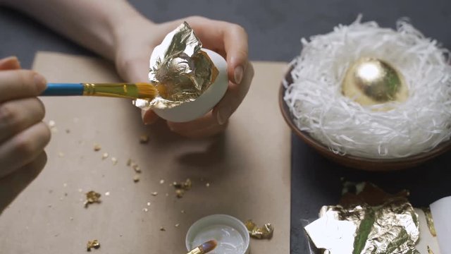 Woman decorates eggs for Easter using gold foil