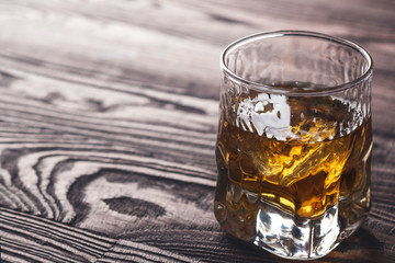 Whiskey with ice in  a glass  on rustic wood background. Copy space