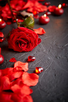 Love and Valentines day concept. Red rose, petals, candles, dating accessories, boxed gifts, hearts, sequins on black stone background, frame composition, top view. Layout for greeting card