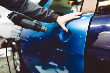 Car wrapping specialist putting vinyl foil or film on car. Selective focus.