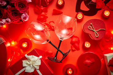 Valentines day romantic decoration with roses, wine glasses, boxed gifts, candles, on a red background table. Top view, copy space.