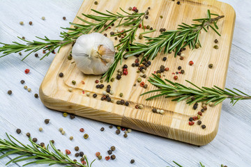 Head of garlic, rosemary branches, spices lie on a cutting board.