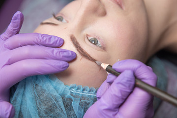 Permanent make-up for eyebrows of beautiful woman with thick brows in beauty salon. Closeup...