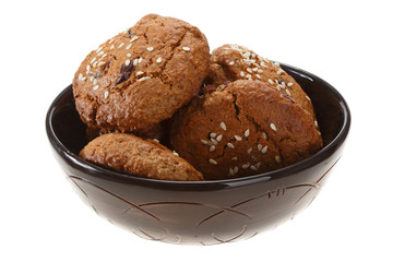 Homemade oatmeal cookies with dried berries and sesame. In a dark shiny clay bowl.  Isolated on white background.