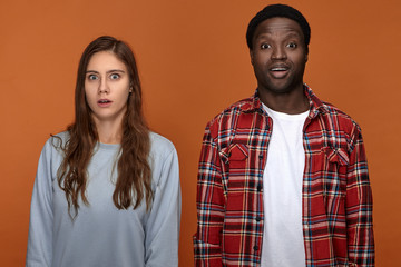 Human facial expressions, emotions, reaction and feelings. Cute funny young interracial couple black guy and white female expressing amazement, opening their mouths, being surprised with news