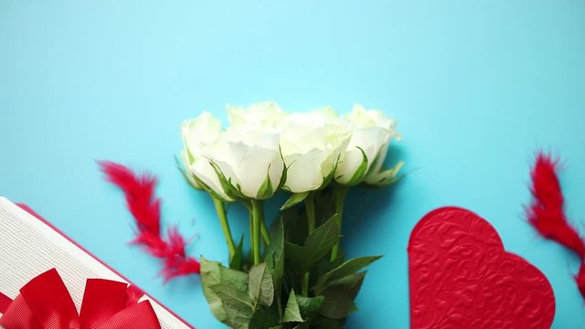 Bouquet of white roses with red bow on blue background. Boxed gift on side. Valentine or love concept image. Floral background image with copy space for text