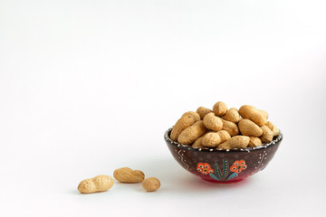 peanuts in shell on clay cup on white background, copy space