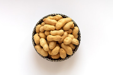 Raw peanuts in shell on clay cup on white background. Top view