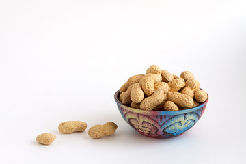 raw peanuts in shell on clay cup, groundnuts on white background. Copy space for text