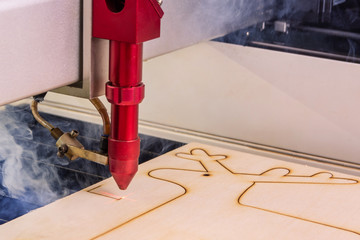 Laser engraver working and engraving wooden board with smoke