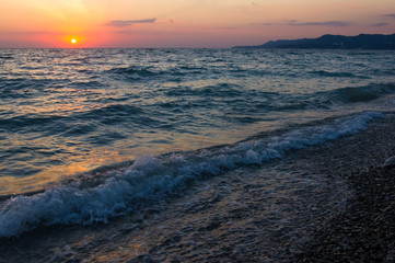 Amazing sea sunset on the pebble beach, the sun, waves, clouds