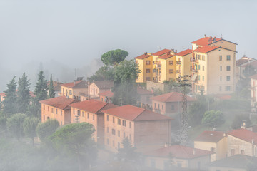 Chiusi Scalo mist fog sunrise of rooftop houses buildings in Umbria, Italy near Tuscany with soft clouds haze covering blanketing town cityscape skyline in summer