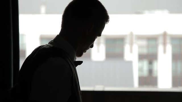 Young man puts on a jacket against the window