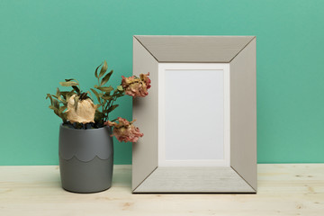 white frame with dry flowers on  desk near green wall