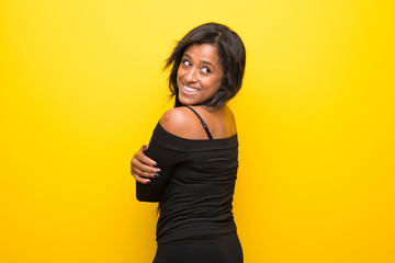 Young afro american woman on vibrant yellow background looking over the shoulder with a smile