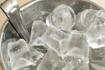 A silver bucket made from aluminum full filled with ice cube is placed on the table at the pub, ice were made for make water, whisky, vodka or alcohol drinking cold