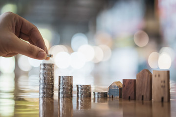 Hand choosing row of coin money on wood table and mini wood house, selective focus, Planning to buy property. Choose what's the best. A symbol for construction ,ecology, loan concepts