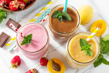 Strawberry, chocolate and apricot milkshake or smoothies on a white wooden background. Healthy juicy vitamin drink diet or vegan food concept.