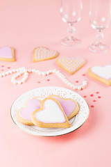 Fototapeta na wymiar Happy Valentine's day greeting card with heart cookies, wine glasses and wine on pastel pink background.