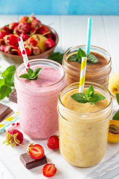 Strawberry, chocolate and apricot milkshake or smoothies on a white wooden background. Healthy juicy vitamin drink diet or vegan food concept.