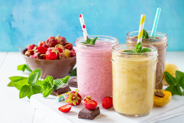 Strawberry, chocolate and apricot milkshake or smoothies on a white wooden background. Healthy...