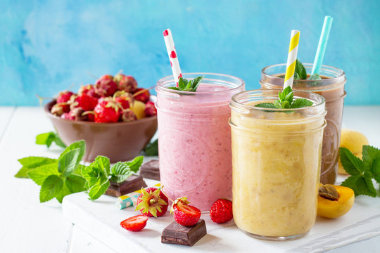 Strawberry, chocolate and apricot milkshake or smoothies on a white wooden background. Healthy juicy vitamin drink diet or vegan food concept. Copy space.