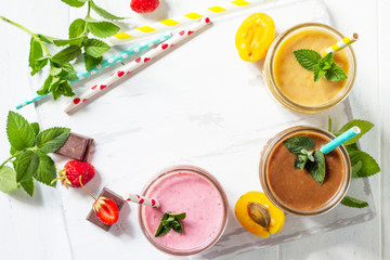 Strawberry, chocolate and apricot milkshake or smoothies on a white wooden background. Healthy juicy vitamin drink diet or vegan food concept. Top view flat lay background, copy space.
