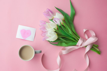 Obraz na płótnie Canvas Bouquet of tulips and a coffee cup on a pink pastel background. Wonderful spring breakfast on Mother's Day or Women. Flat lay. View top. Selective focus.