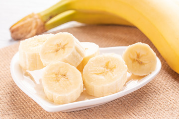 Sliced and whole bananas on a white plate and old wooden roofing